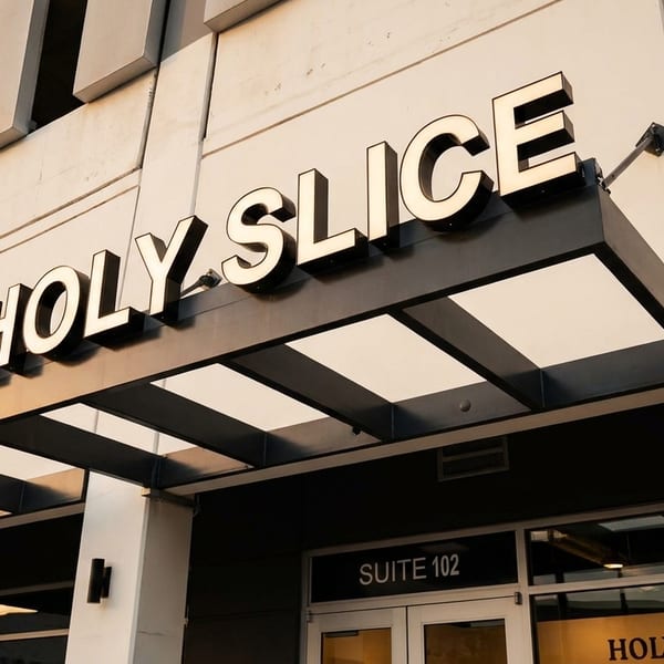 The Holy Slice restaurant sign with white letters on a dark background, above the entrance.