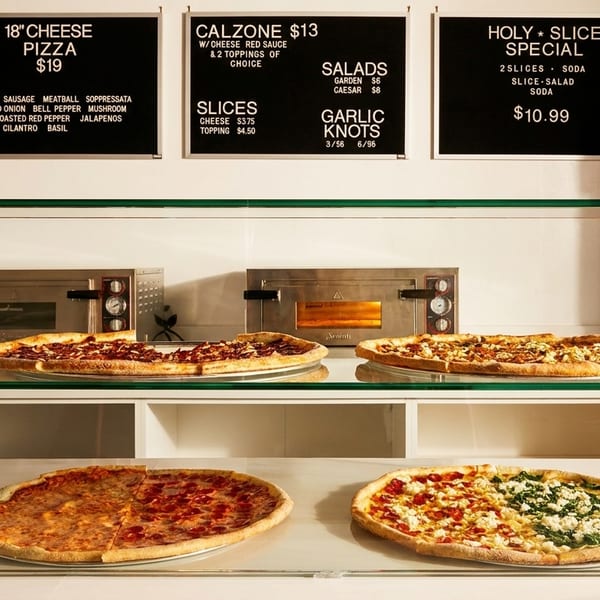 A glass display case shows four pizzas, with menu boards for Holy Slice above.