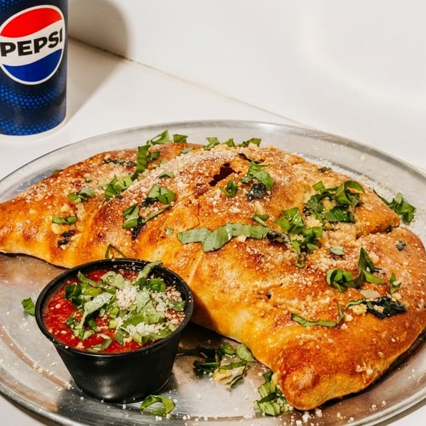 A golden-brown calzone with herbs and parmesan, served with marinara sauce and a Pepsi.
